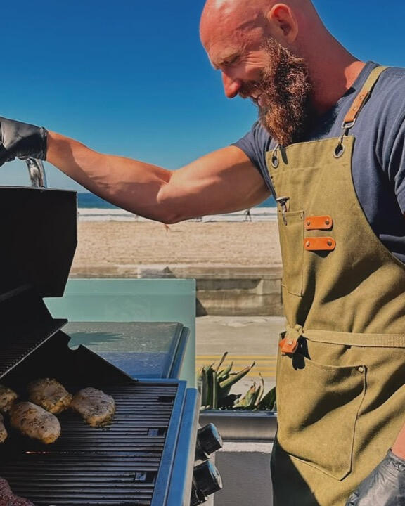 Reid cooking over an outdoor grill Private chef Reid Armstrong grilling by the ocean in San Diego